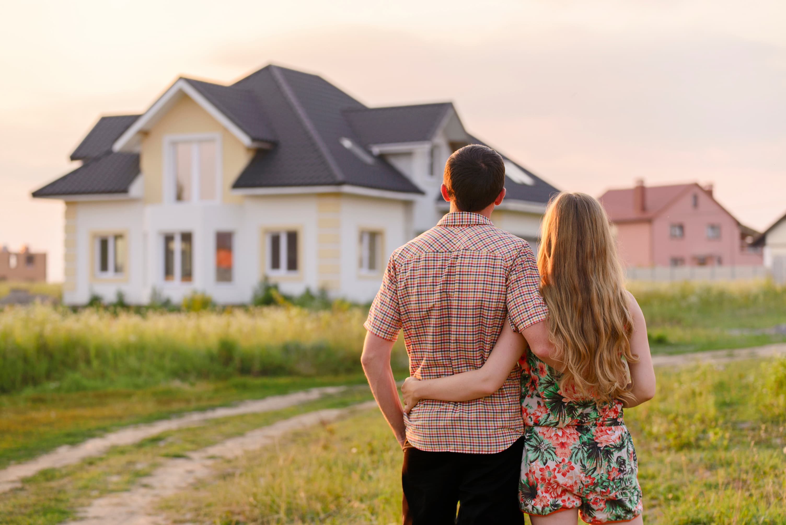 A young couple stands together outside their first home at sunset